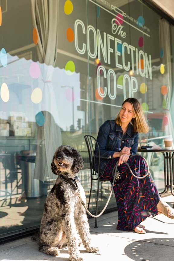 A woman sits outside a store with a dog.
