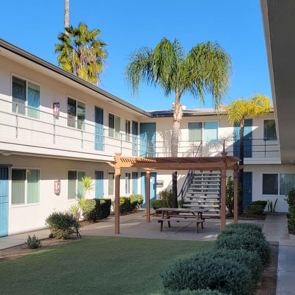 a courtyard with a picnic bench and palm trees in front of a white building