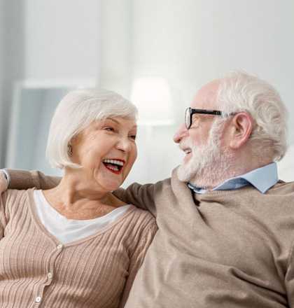 an older man and woman sitting on a couch laughing