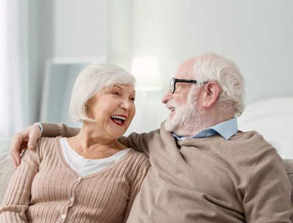 an older man and woman sitting on a couch laughing