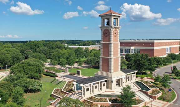 A large building with a clock tower is surrounded by trees and greenery.