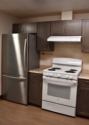 A kitchen with a stainless steel refrigerator, a white stove, and brown cabinets.