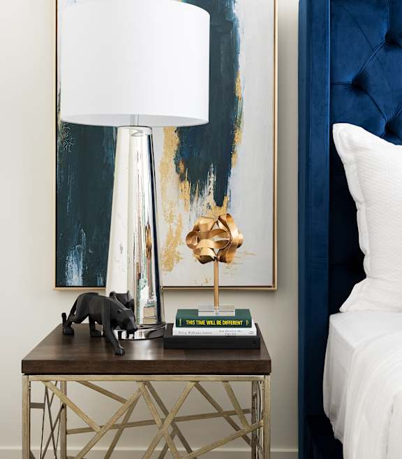 A table with a lamp and a painting on the wall.