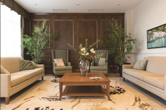 A living room with coffee table with flower arrangement and comfortable chairs and couches.