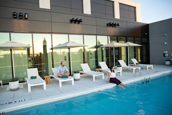 A woman is sitting on the edge of a pool. at Scout Living, powered by Placemakr Apartments, Atlanta, GA, 30308