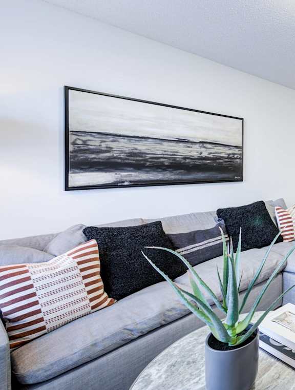 A living room with a grey couch and a painting on the wall.