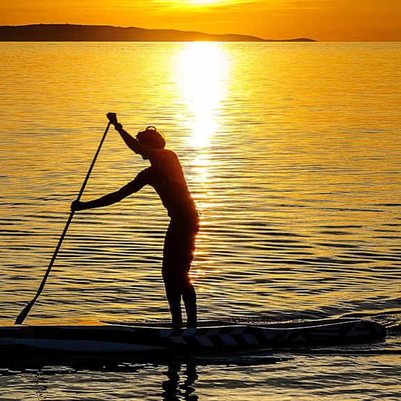 A person paddleboarding on a calm body of water during sunset.