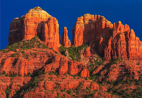 A large red rock formation with greenery on top stands tall against a blue sky.