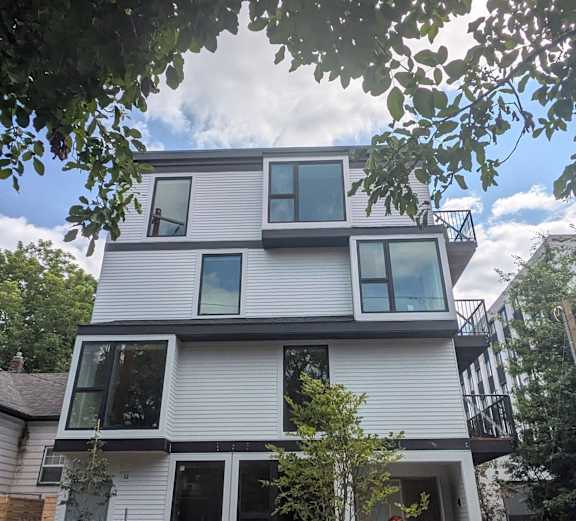 A modern house under construction with white siding and large windows.
