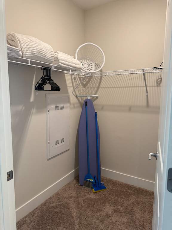 A small, white closet with a fan and a blue vacuum cleaner.