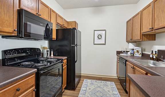Fully equipped kitchen with black appliances and wood cabinetry in Tattersall Village Apartments, Hinesville, GA