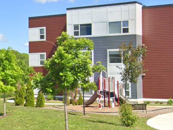 A playground with a slide and a tree in front of a building.