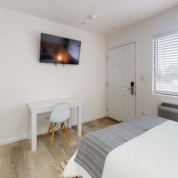 A bedroom with a bed, desk, chair, and a television mounted on the wall.
