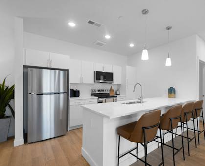 A modern kitchen with a white island and brown barstools.