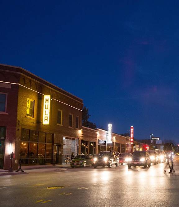 A street scene at night with cars and pedestrians.