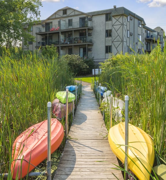 A wooden walkway with canoes on either side leads to a building at Medicine Lake Apartments, Plymouth, Minnesota.