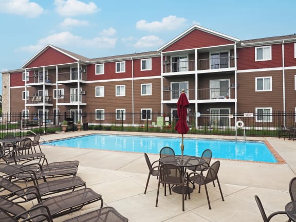 an outdoor pool area with tables and chairs near an apartment building