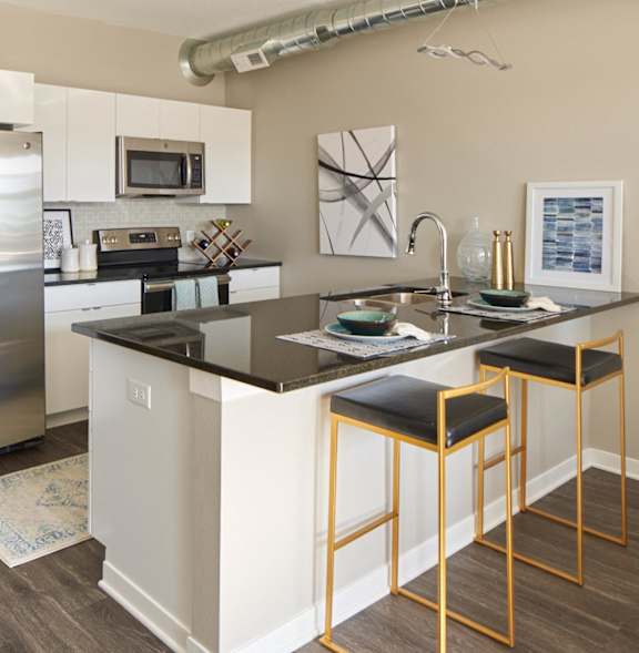 A kitchen with a refrigerator, microwave, and bar stools.