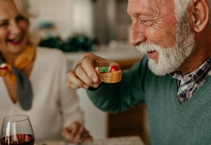 A man is eating a small pastry while sitting at a table with a glass of red wine.