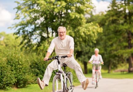 An elderly man is riding a bicycle in a park.