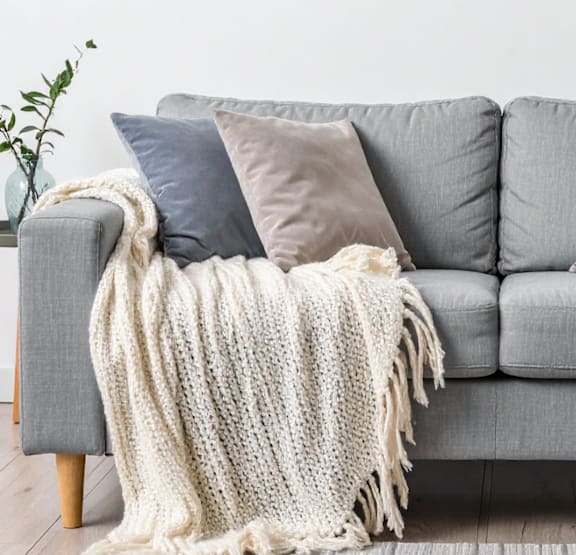 A grey couch with a white knitted throw draped over it.