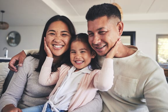 A family of three is sitting closely together, sharing a joyful moment.