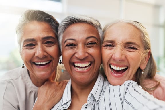 Three women are laughing together in a bright room.