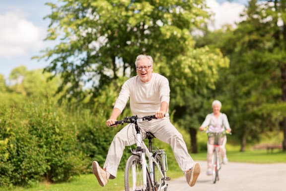 An elderly man is riding a bicycle in a park.