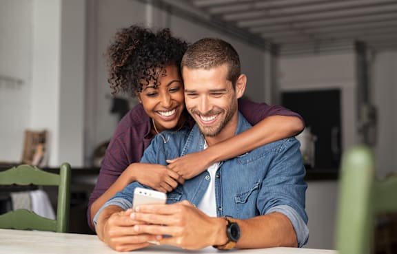 A man and woman are sitting at a table looking at a smartphone.