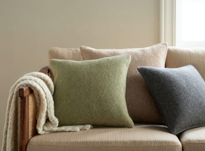 A beige couch with a green pillow and a brown throw blanket.