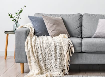 A grey couch with a white knitted throw draped over it.
