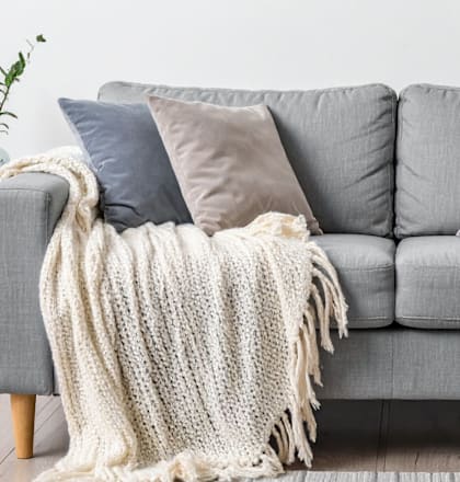 A grey couch with a white knitted throw draped over it.