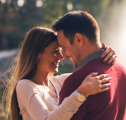 A couple in a red sweater and white shirt are embracing each other.