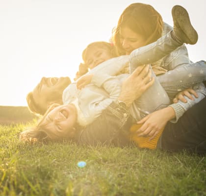 A family of three is lying on the grass in the sunlight.
