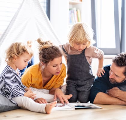 A family of four is sitting on the floor reading a book together.