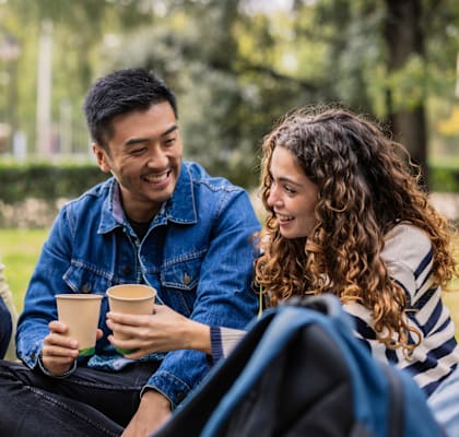 Three friends are sitting on the grass, enjoying a conversation and drinks.