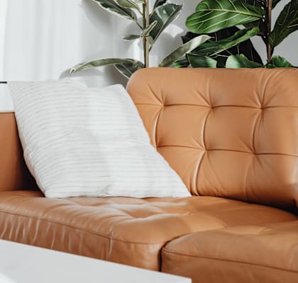 A white pillow on a tan leather couch.