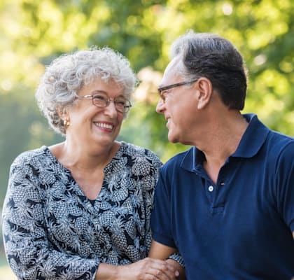 An elderly couple holding hands and smiling in a park.