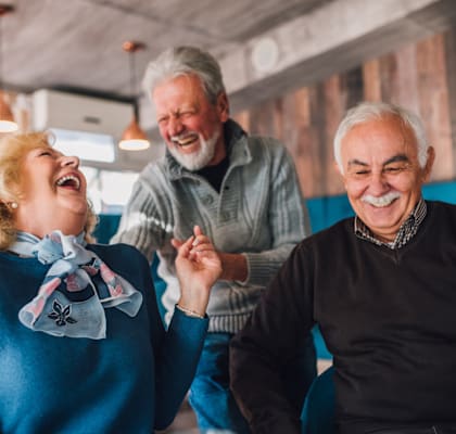 Three elderly people are laughing together in a room with a brick wall.