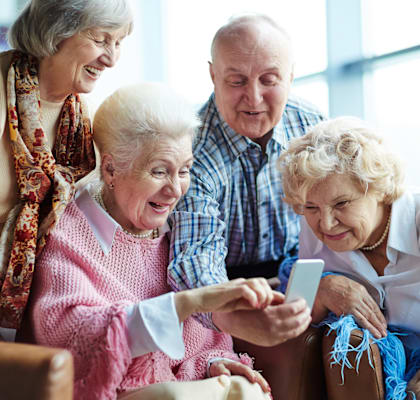 A group of elderly people are gathered around a table, looking at a smartphone.