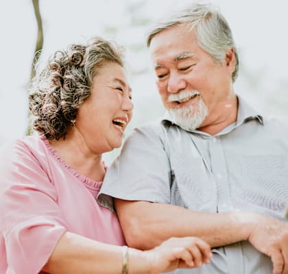 An elderly couple is sitting on a bench with a tablet in the man's hand.