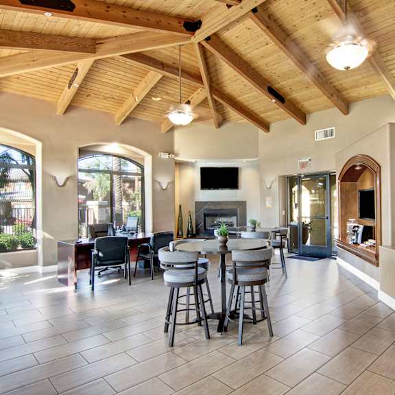 The front office at Reserve at Arrowhead with a desk, a desktop, a TV, a fireplace, high tables, and barstool chairs.