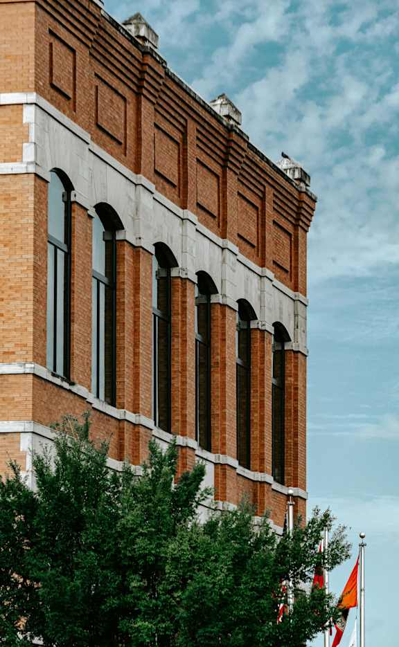 A brick building with flags and a tree beside it.