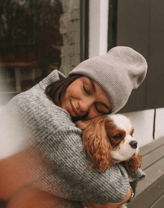 A person in a grey beanie is holding a small brown dog.