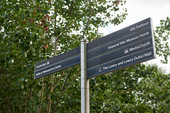 A signpost with directions to various locations such as Anchorage, Saltford Water Sports Centre, Old Trafford, Imperial War Museum North, MediaCityUK, The Lowry and Lowry Outlet.