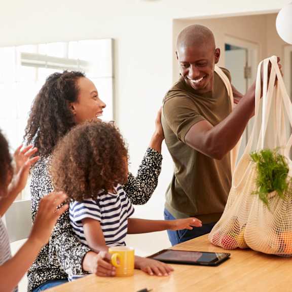 A man is holding a bag with vegetables and fruits in front of a family.
