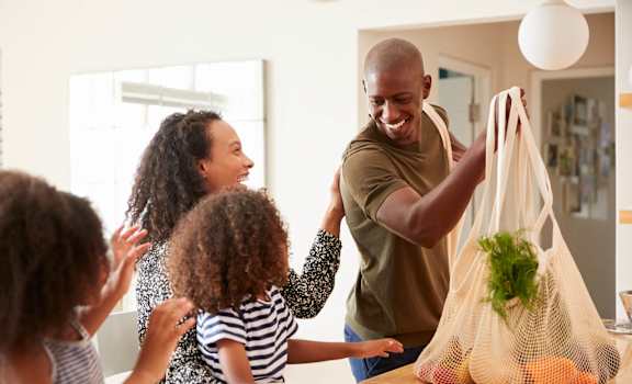 A man is holding a bag with vegetables and fruits in front of a family.
