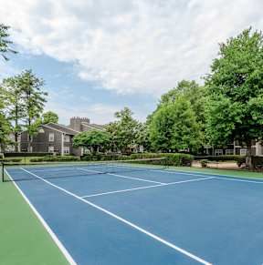 A blue tennis court surrounded by green trees and buildings.