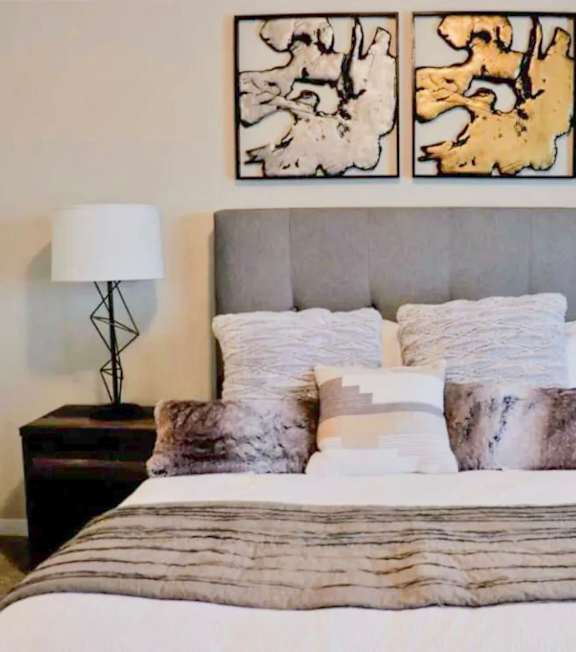 A bedroom with a bed, two lamps, and two paintings on the wall.