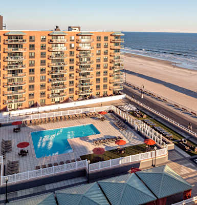 A view of a beachfront hotel with a swimming pool and beach access. at 10 West Apartments, Long Beach, New York